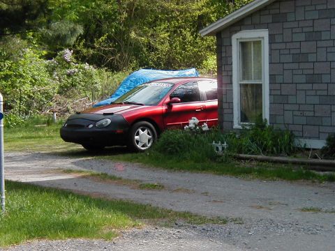 1997 Ford Taurus - A red sedan, likely a 1996 model, is parked on a gravel driveway beside a house.