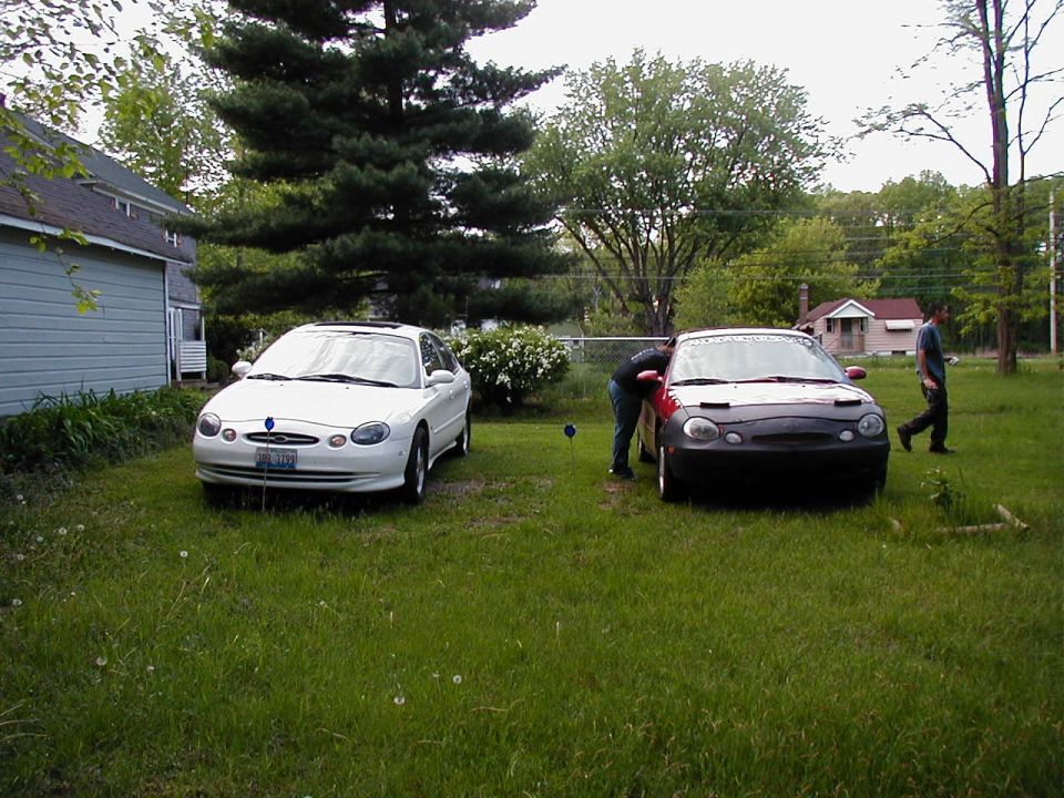 Two 1997 Ford Taurus sedans parked in a yard, one white, one red with a black car bra