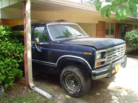 1981 Ford Bronco - Dark blue Ford Bronco parked under a carport, front quarter view. The hood is slightly ajar.