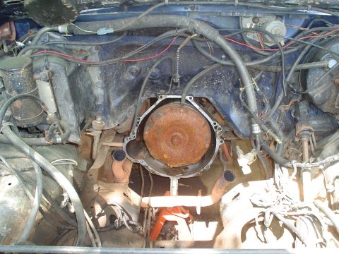 1981 Ford Bronco - The engine bay of a vehicle is shown with the transmission removed, revealing the torque converter and exhaust manifolds.