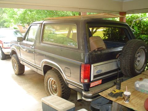 1981 Ford Bronco - This Ford Bronco is parked under a carport, carrying lumber on its roof. A second vehicle is visible to the left.