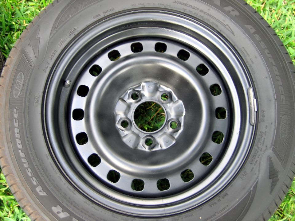 Black steel wheel mounted on a Goodyear Assurance tire lying flat on grass