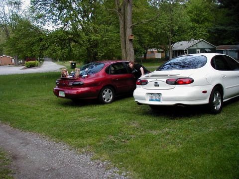 1997 Ford Taurus - Two sedans are parked on a grassy area, one red and one white, with a person leaning into the red car.