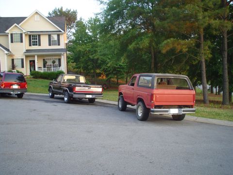 1981 Ford Bronco - Two older model Ford trucks are parked on a residential street in front of a house.