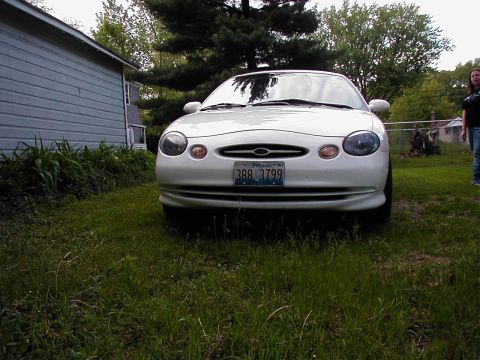 1997 Ford Taurus - A white sedan is parked on a grassy lawn in front of a light blue house.