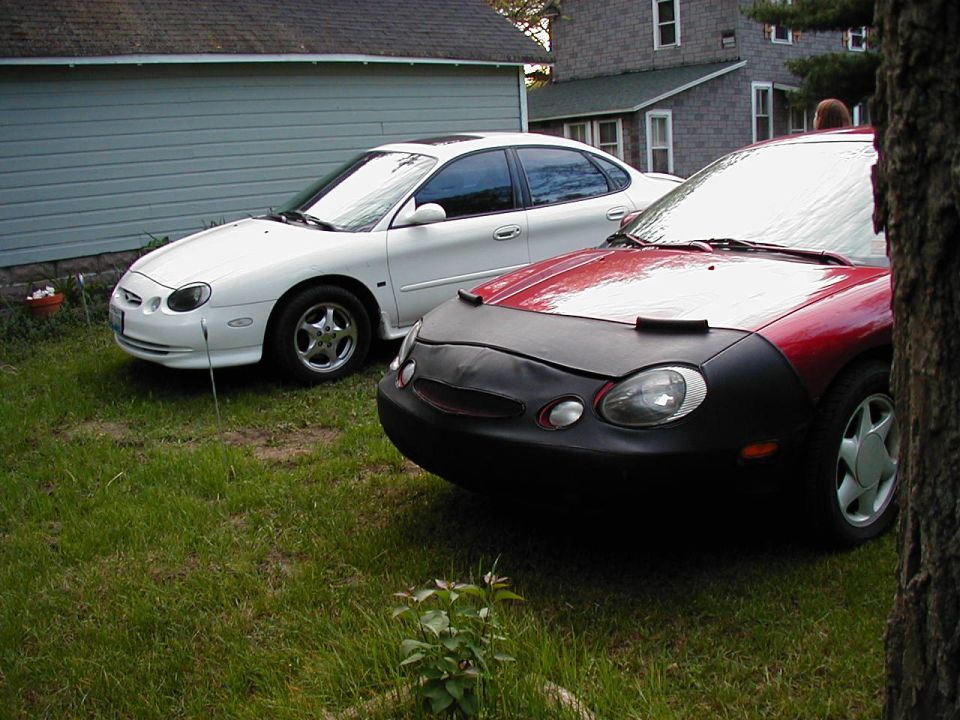 White 1997 Ford Taurus parked next to a red car with a car bra