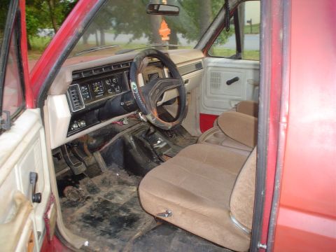1981 Ford Bronco - The interior of a red truck, likely from the early 1980s, shows worn tan seats and a cluttered dashboard.