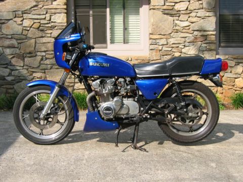 1985 Ford Crown Victoria LTD - A blue Suzuki motorcycle is parked on a concrete surface in front of a stone wall and a window.