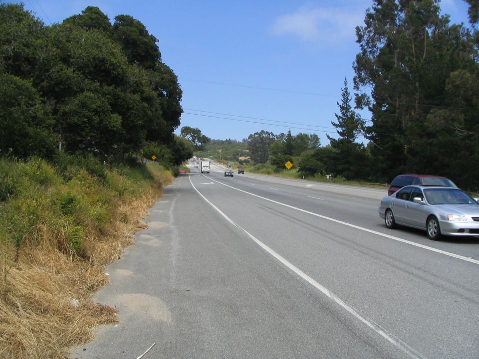 Silver sedan and dark SUV driving on a highway with trees and blue sky