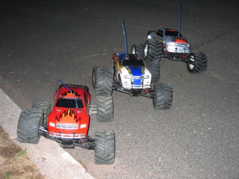 1996 Ford Crown Victoria - Three remote control monster trucks with flame decals are positioned on a paved surface.