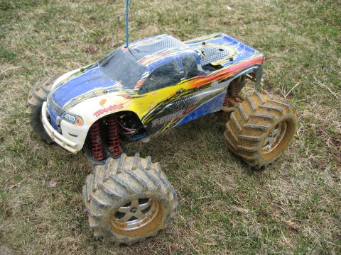 1996 Ford Crown Victoria - A remote control monster truck with a detached wheel sits on grassy terrain, showing off its mud-caked tires and vibrant decals.