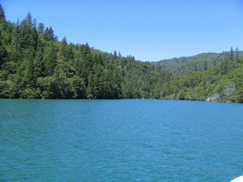 blue lake water with tree-covered hills under a clear sky. Supermotors logo in corner