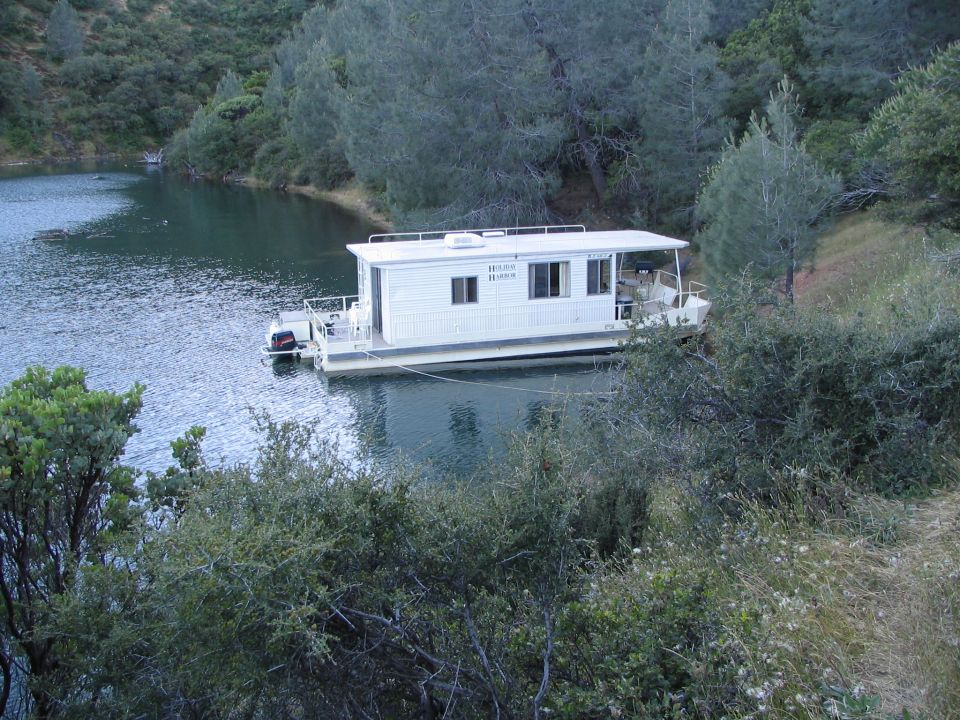 White houseboat on a lake, with trees and hills in the background