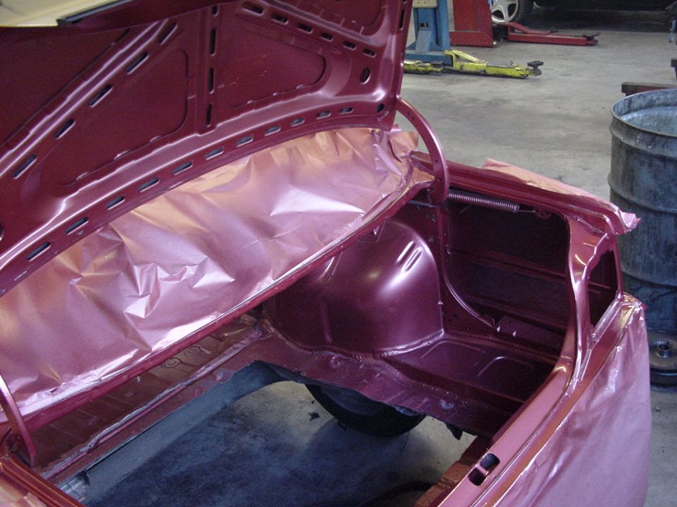 Maroon car trunk interior with plastic sheeting, showing structural details and a spare tire well