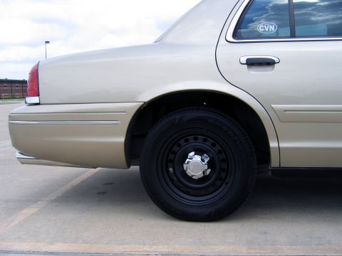 2000 Ford Crown Victoria - Side view of a tan sedan's rear quarter panel and wheel, with a 'CVN' sticker on the window.