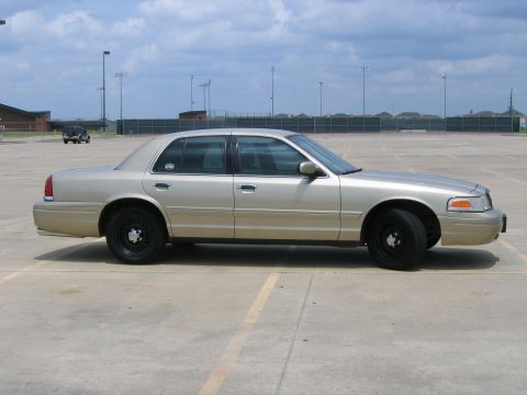 2000 Ford Crown Victoria - A gold 2000 Ford Crown Victoria sedan is parked in an empty lot under a cloudy sky.