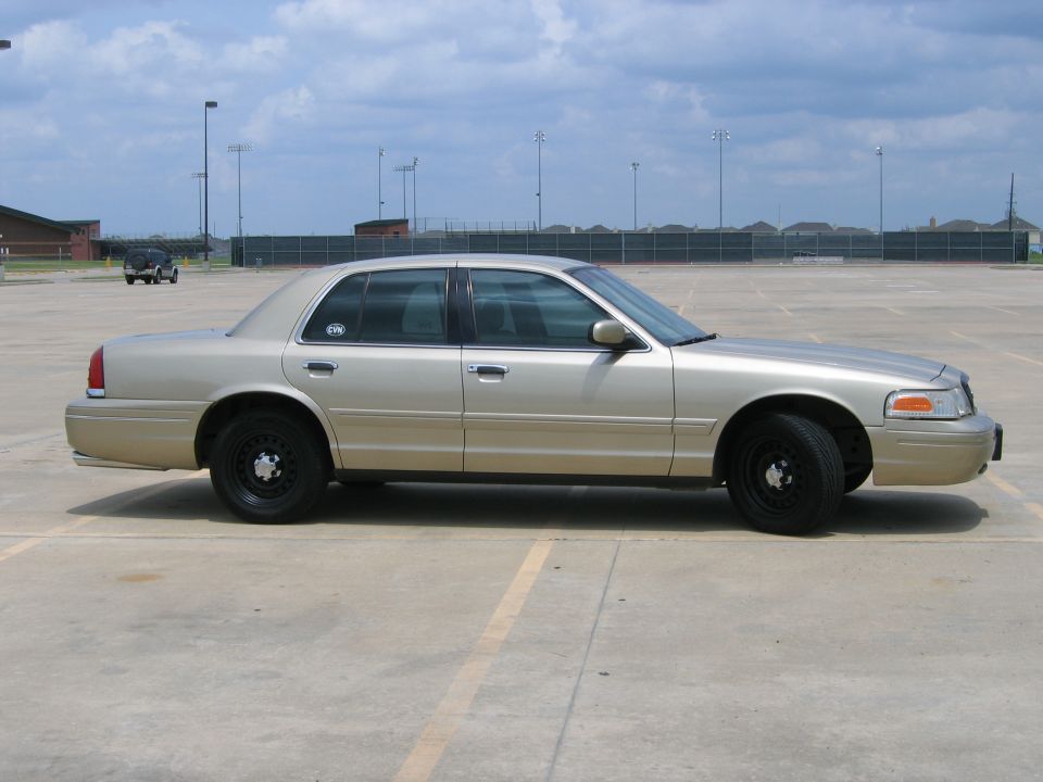 Gold Ford Crown Victoria sedan side view on black steel wheels in an empty parking lot