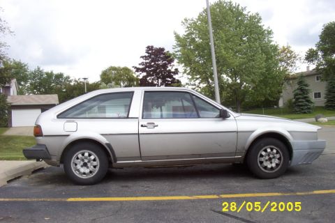 1983 Volkswagen Scirocco - A silver Volkswagen Scirocco is parked in a lot with a residential building and trees in the background.