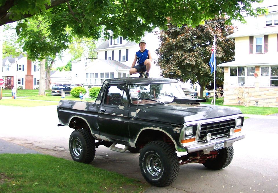 Boy sitting atop the roof of a lifted black Ford Bronco parked on a residential street