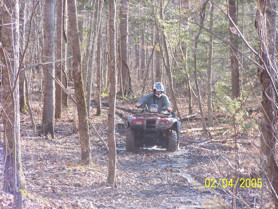 Rider on red ATV navigating muddy forest trail in winter