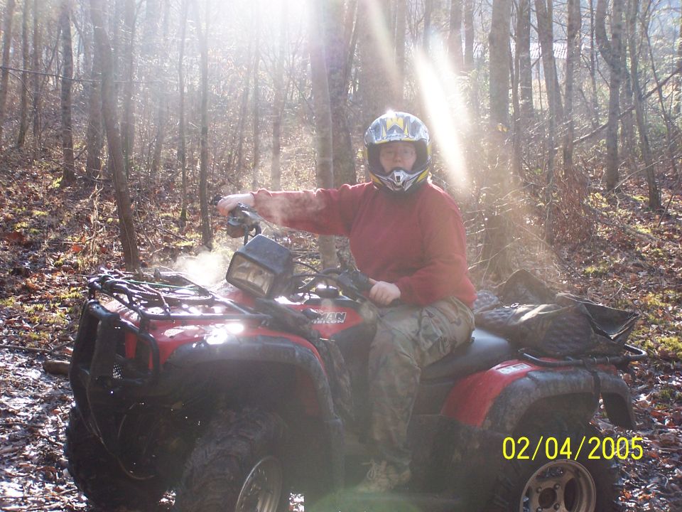 Red Honda Rubicon ATV with rider in helmet on a wooded trail