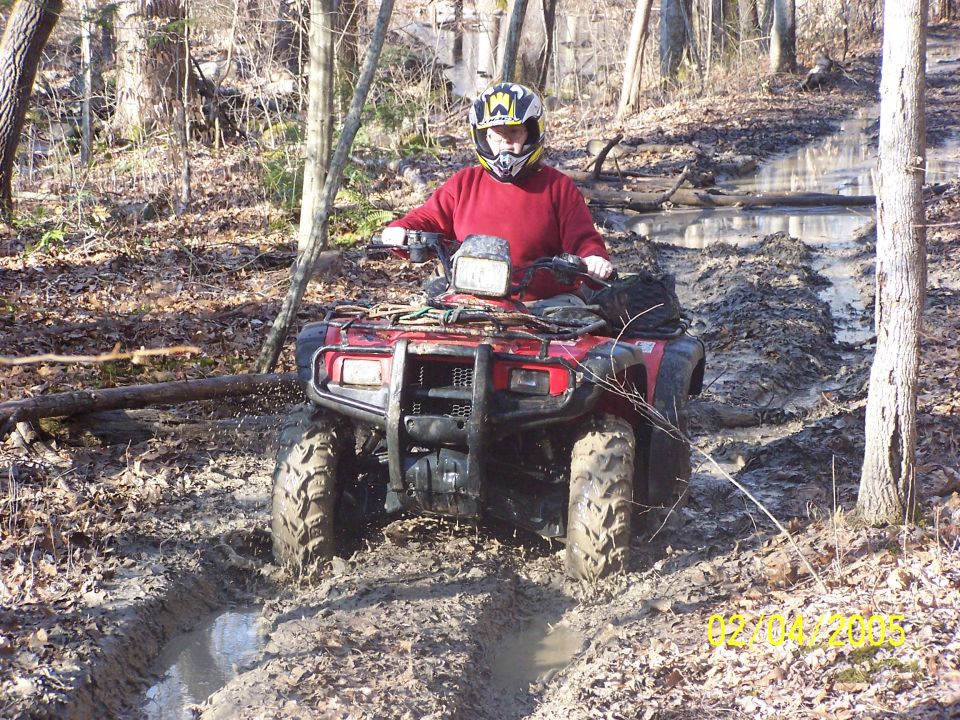 Red Honda ATV ridden through deep mud on a wooded winter trail