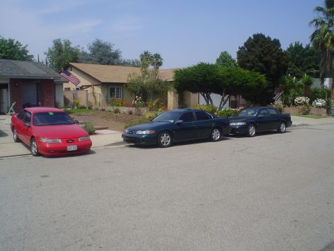 1993 Ford Taurus - Three sedans are parked in a residential area on a sunny day.