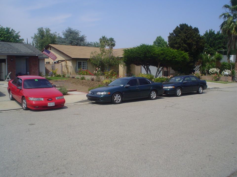 red sedan and two dark sedans parked on street in front of houses