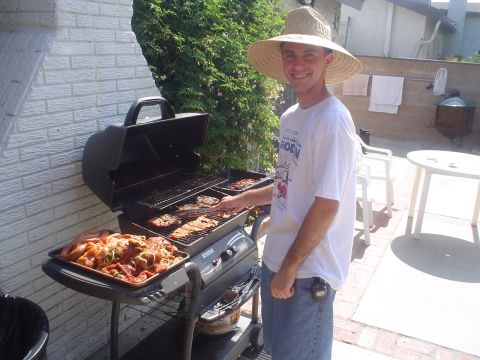 1993 Ford Taurus - A man wearing a wide-brimmed straw hat grills food in a backyard setting.