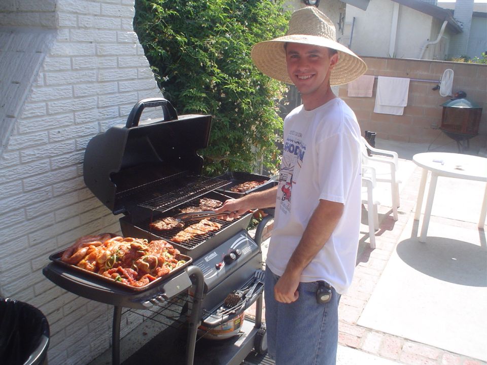Man in straw hat grilling meat and vegetables on a barbecue in a backyard