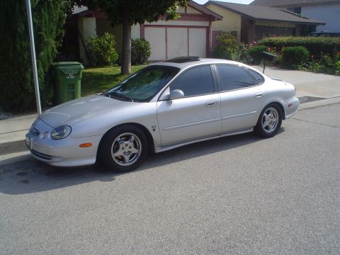 1993 Ford Taurus - A silver sedan is parked on the side of a street in front of a house.