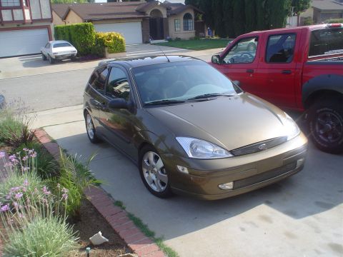 1993 Ford Taurus - A gold Ford Focus hatchback is parked on a driveway next to a red pickup truck.