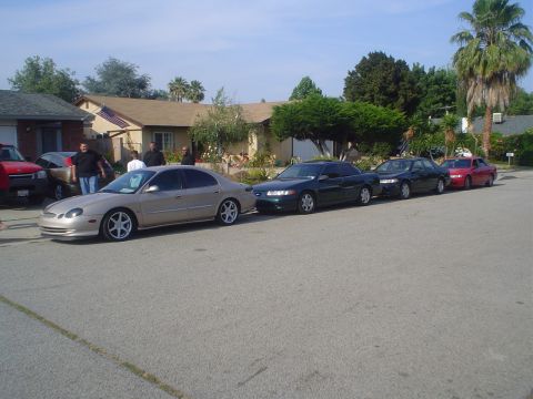 1993 Ford Taurus - A line of sedans is parked on a residential street, with the closest vehicle being a tan sedan.