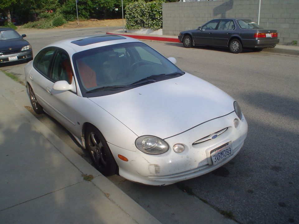 White Ford Taurus parked on street, another car in background