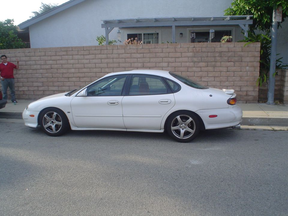 White sedan parked on street, side view. Damage on rear bumper