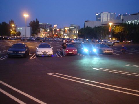 1993 Ford Taurus - Several cars parked in a lot at dusk, with a shopping center visible in the background.