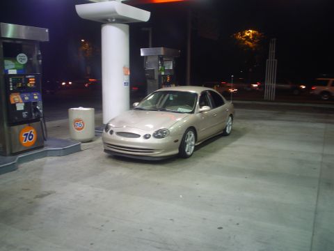 1993 Ford Taurus - A tan sedan is parked at a gas station at night, with the gas pumps visible to the left.