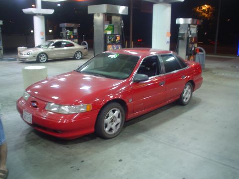 1993 Ford Taurus - A red sedan is parked at a gas pump at night, with another car visible in the background.