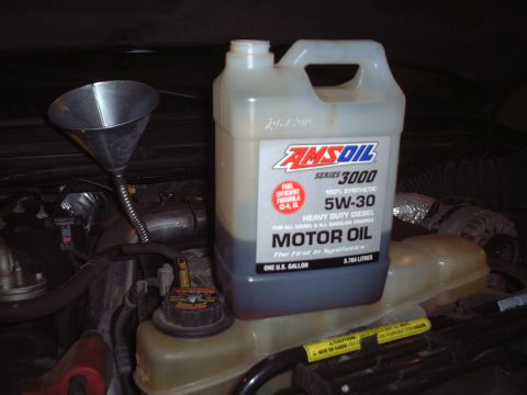 2000 Ford Excursion - A jug of AMSOIL Series 3000 5W-30 Heavy Duty Diesel motor oil sits in the engine bay next to a funnel.