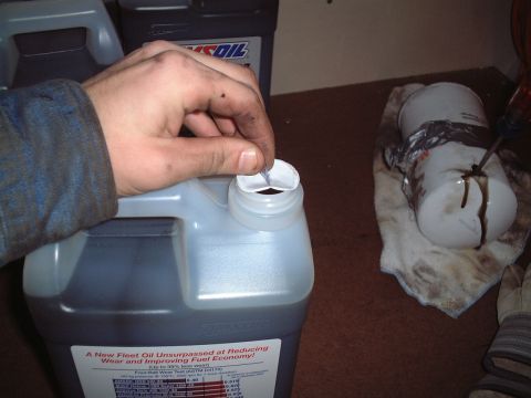 2000 Ford Excursion - A person is opening a jug of AMSOIL oil, with a used oil filter and rags nearby.