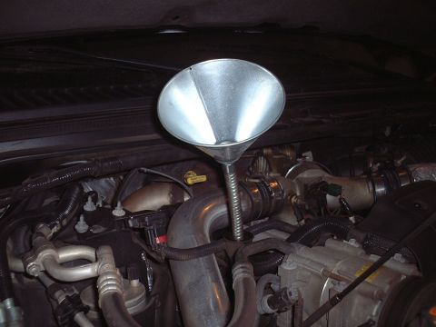 2000 Ford Excursion - A metal funnel is positioned in the engine bay of a 2000 Ford Excursion for an oil change.