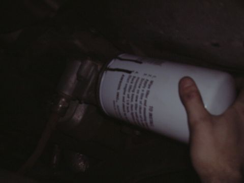 2000 Ford Excursion - A hand installs a white oil filter with black text, likely during an oil change.