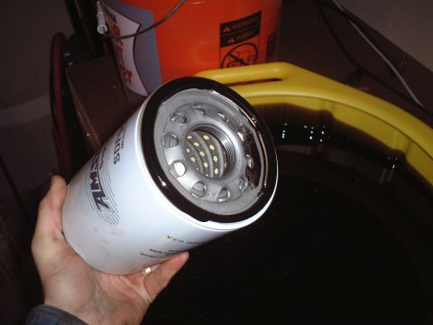 2000 Ford Excursion - A new AMSOIL oil filter is held above a drain pan containing used motor oil, ready for an oil change.
