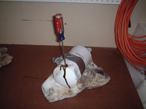 2000 Ford Excursion - A screwdriver is used to puncture an oil filter, causing oil to drain onto a rag.