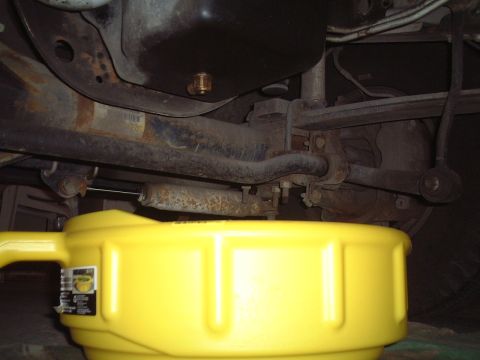 2000 Ford Excursion - A yellow oil drain pan is positioned beneath the rusty undercarriage of a vehicle, ready to catch used oil.