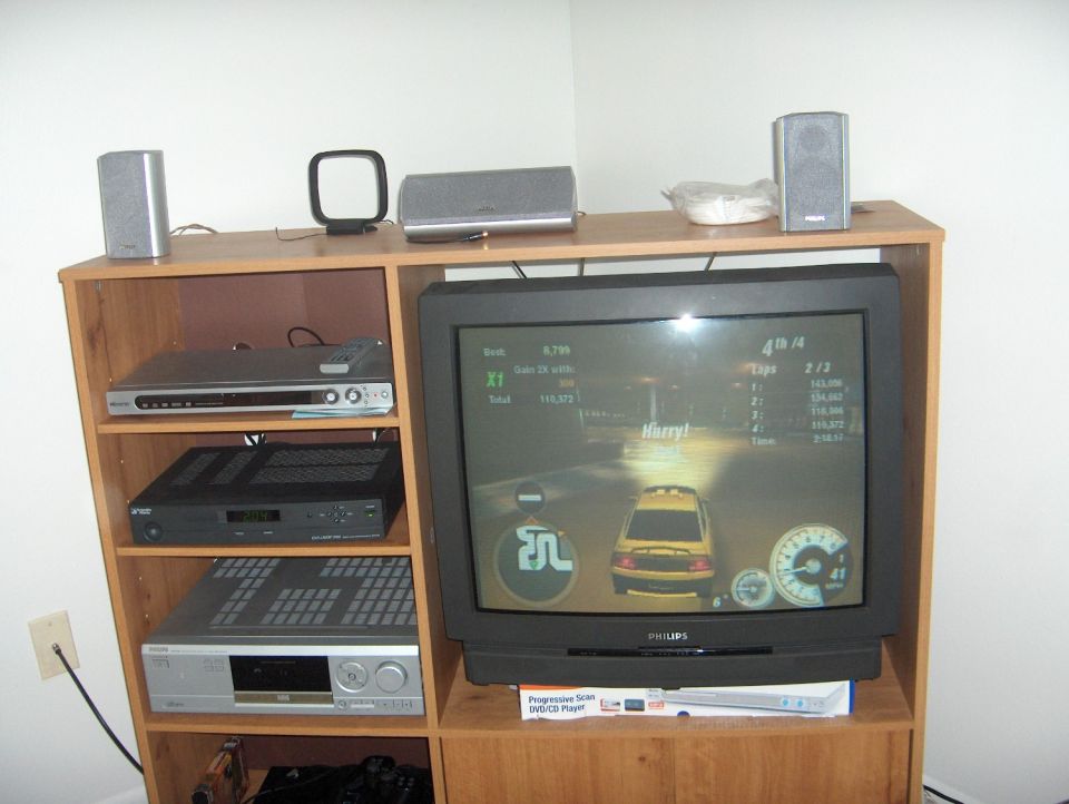 CRT TV showing racing game in wooden entertainment center with speakers and A/V gear