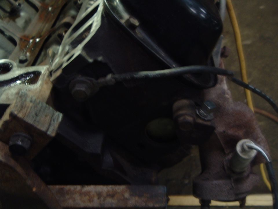 Rear of a disassembled V8 engine block on a stand with rusty manifold and O2 sensor