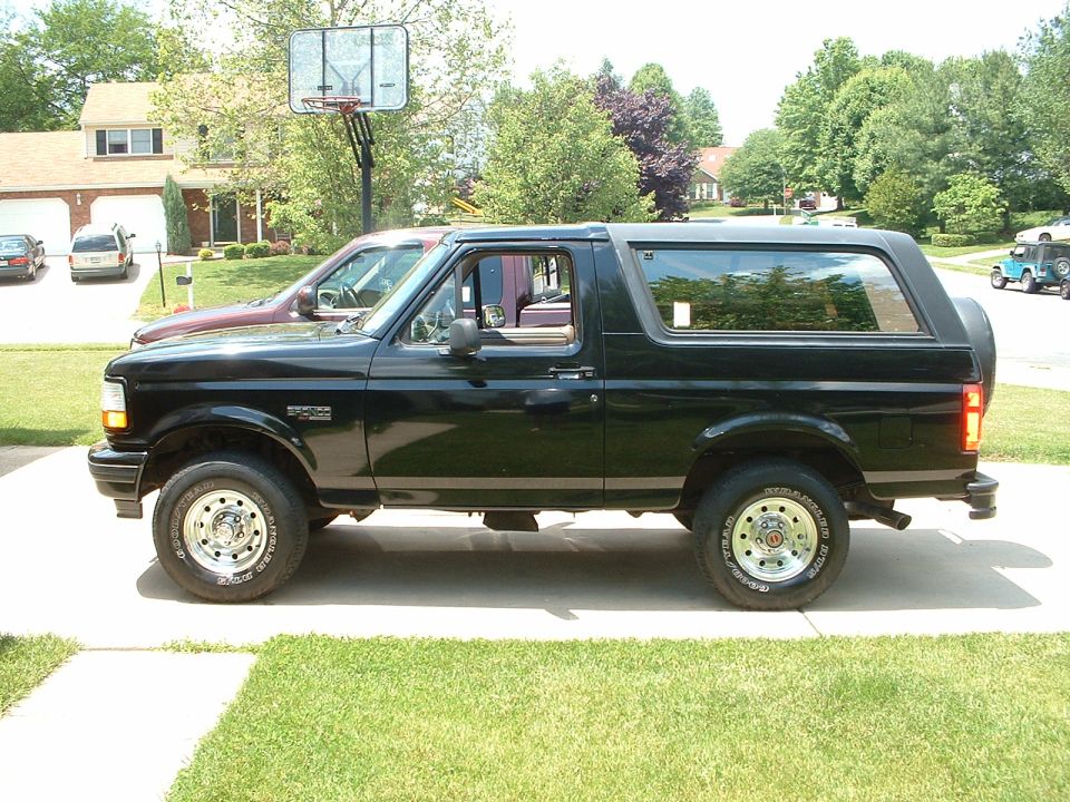 Black Ford Bronco parked in driveway, another car behind it, house and basketball hoop in background