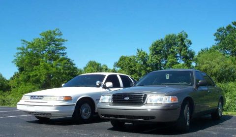 1998 Ford Crown Victoria - Two Ford Crown Victorias are parked side-by-side on a sunny day with trees in the background.