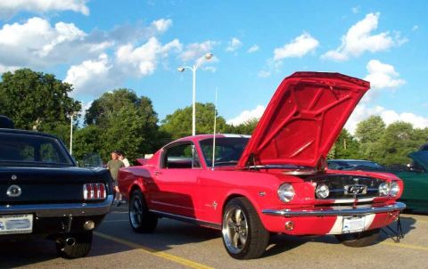 1998 Ford Crown Victoria - A bright red classic Mustang is displayed with its hood up at an outdoor car show.